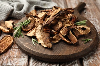 Photo of Dried chanterelle mushrooms with rosemary on wooden table, closeup