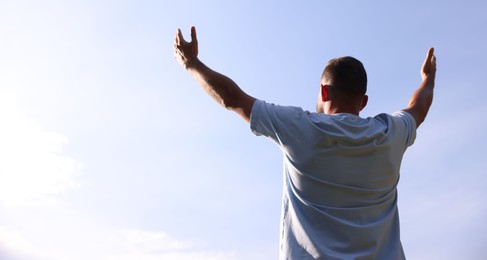 Photo of Feeling freedom. Man enjoying time outdoors against blue sky, back view. Space for text