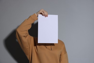 Photo of Anonymity. Woman hiding behind blank paper sheet on light grey background