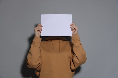 Photo of Anonymity. Woman hiding behind blank paper sheet on light grey background