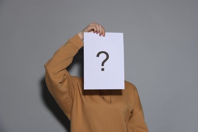 Photo of Anonymity. Woman hiding behind paper sheet with question mark on light grey background