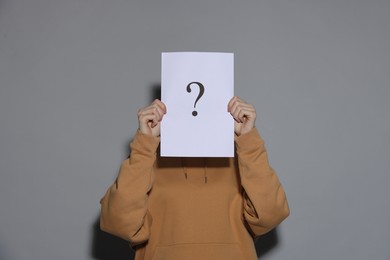 Photo of Anonymity. Woman hiding behind paper sheet with question mark on light grey background