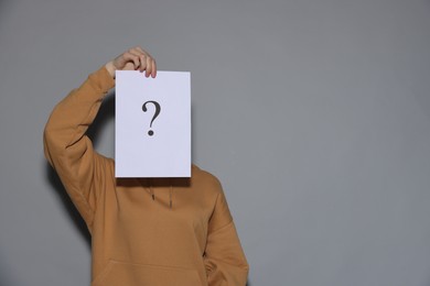 Photo of Anonymity. Woman hiding behind paper sheet with question mark on light grey background, space for text