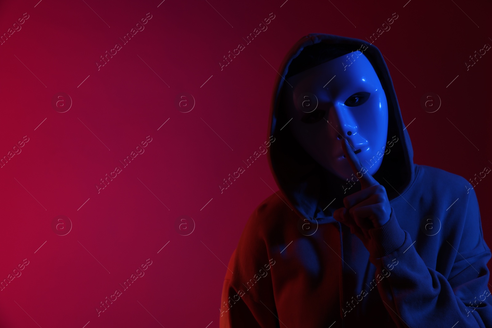 Photo of Anonymity. Woman wearing mask and showing hush gesture on burgundy background in blue light, space for text