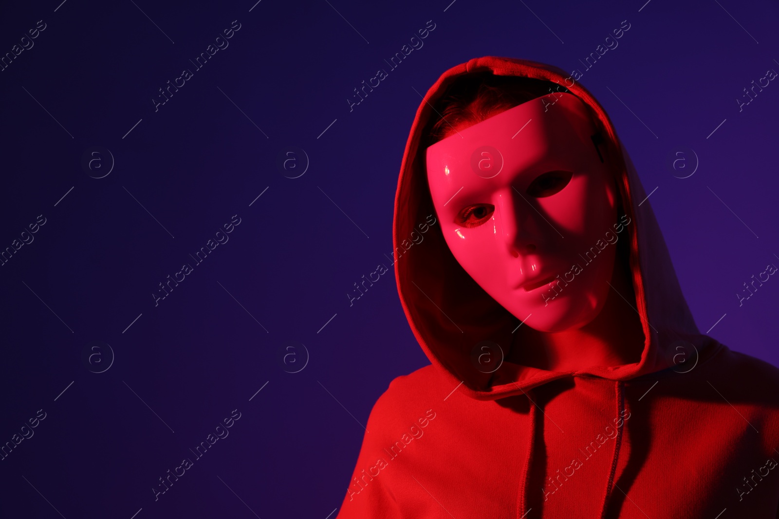 Anonymity. Woman wearing mask on dark blue background in red light, space for text Photo of Anonymity. Woman wearing mask on dark blue background in red light, space for text