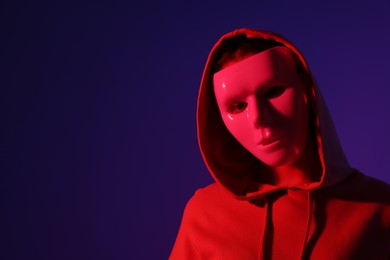 Photo of Anonymity. Woman wearing mask on dark blue background in red light, space for text