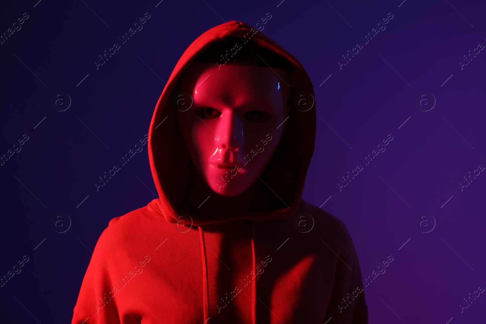 Anonymity. Woman wearing mask on dark blue background in red light Photo of Anonymity. Woman wearing mask on dark blue background in red light