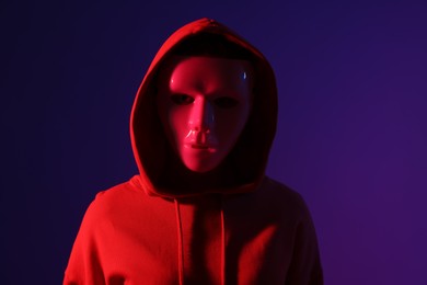 Photo of Anonymity. Woman wearing mask on dark blue background in red light
