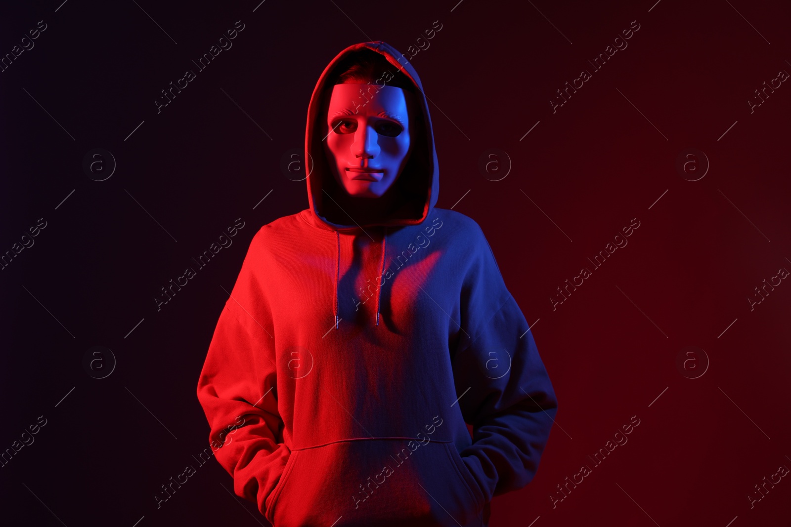 Anonymity. Woman wearing mask on dark red background in neon lights Photo of Anonymity. Woman wearing mask on dark red background in neon lights