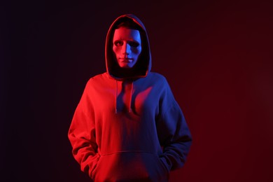 Photo of Anonymity. Woman wearing mask on dark red background in neon lights