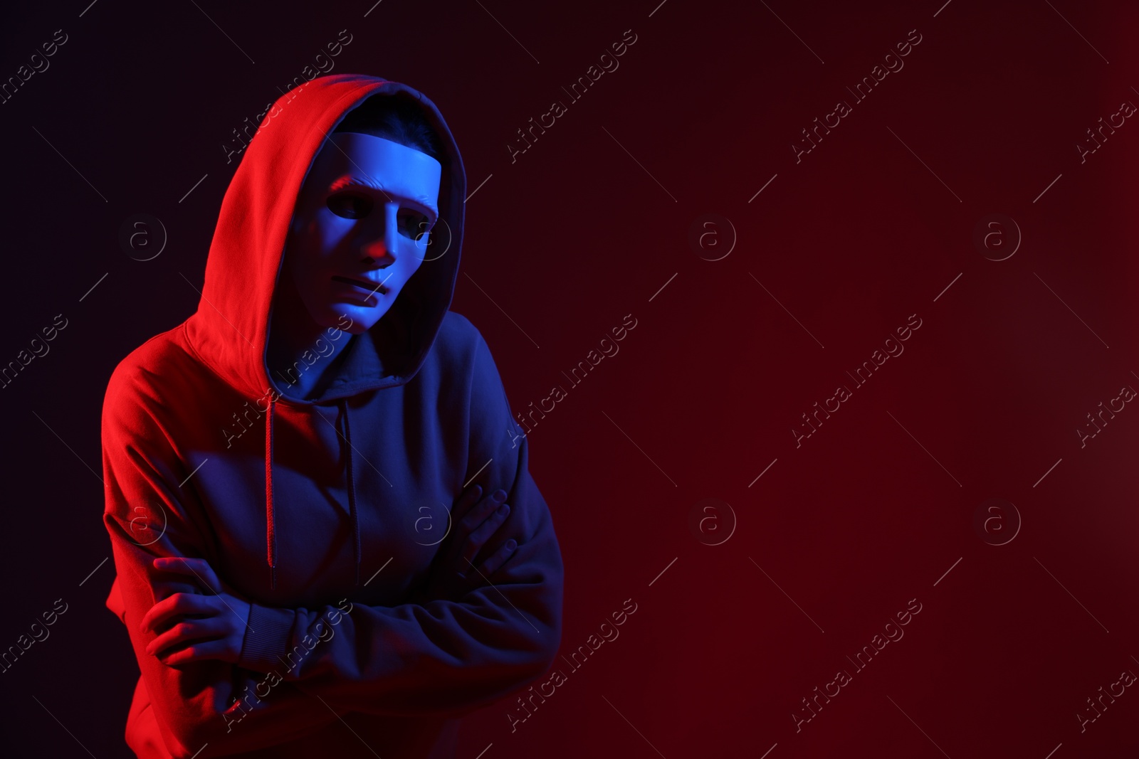 Anonymity. Woman wearing mask on dark red background in neon lights, space for text Photo of Anonymity. Woman wearing mask on dark red background in neon lights, space for text