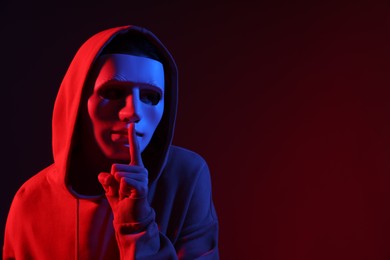 Photo of Anonymity. Woman wearing mask and showing hush gesture on dark red background in neon lights, space for text