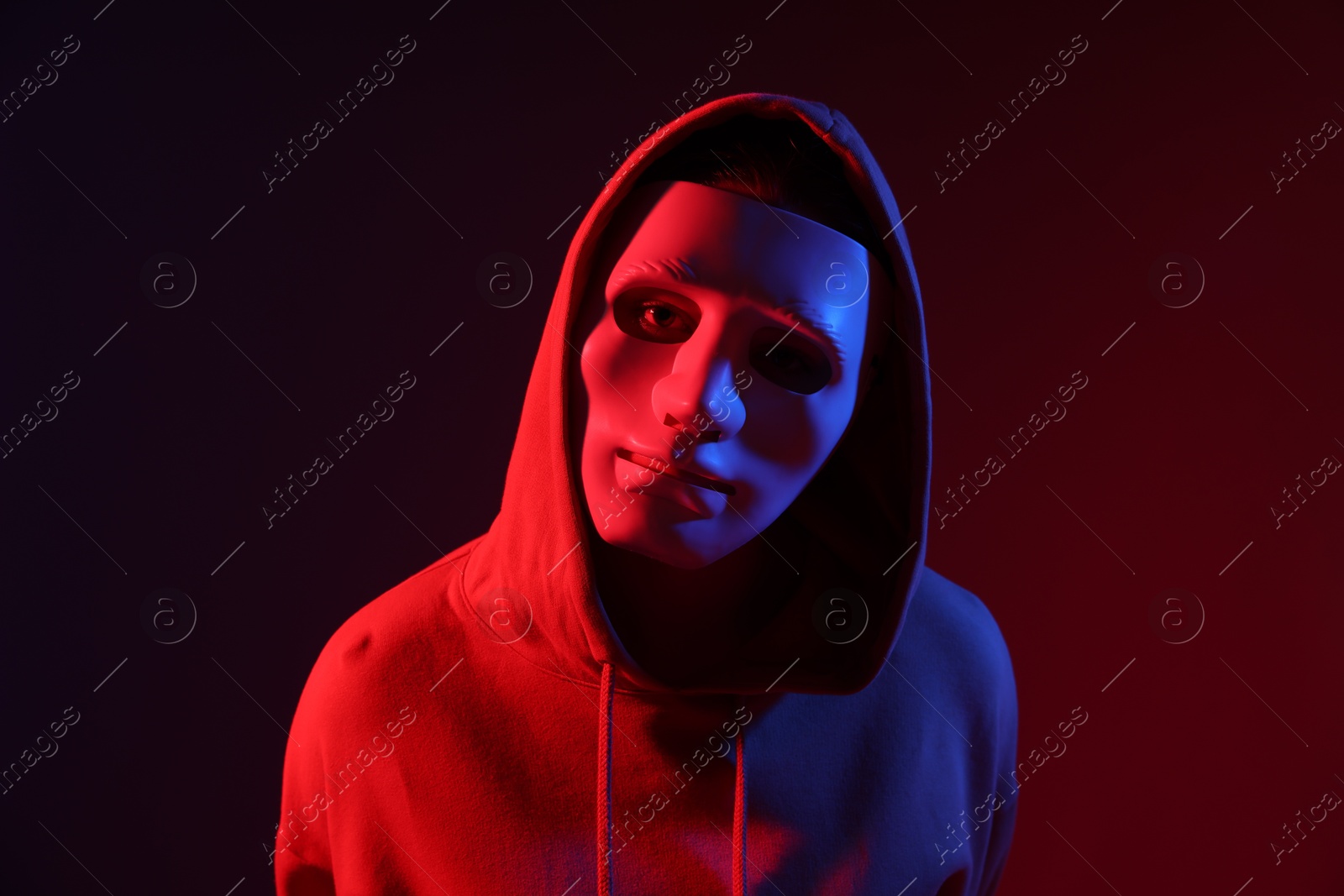 Anonymity. Woman wearing mask on dark red background in neon lights Photo of Anonymity. Woman wearing mask on dark red background in neon lights