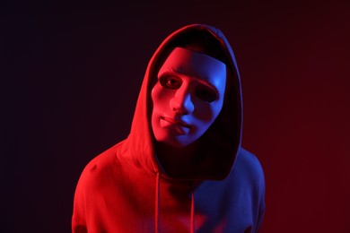 Photo of Anonymity. Woman wearing mask on dark red background in neon lights