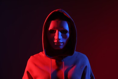 Photo of Anonymity. Woman wearing mask on dark red background in neon lights