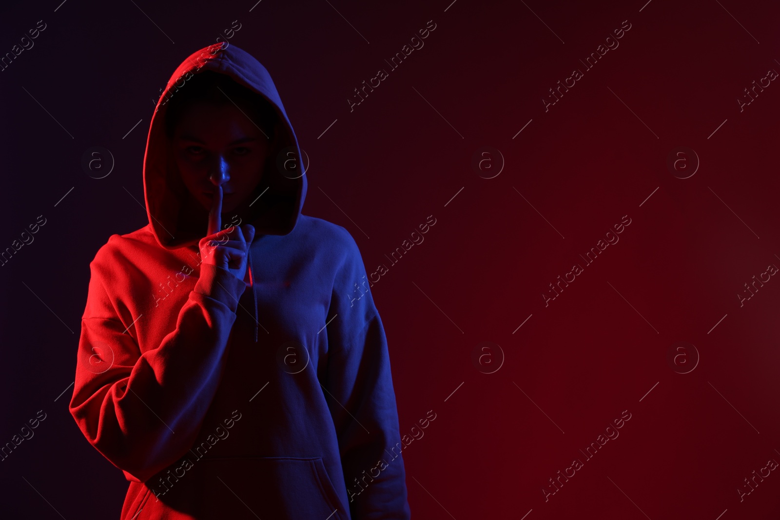 Photo of Anonymity. Woman hiding her face and showing hush gesture on dark red background, space for text