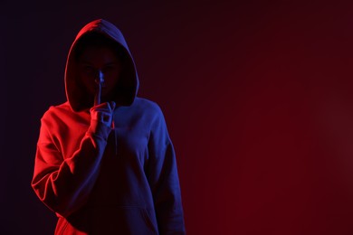 Photo of Anonymity. Woman hiding her face and showing hush gesture on dark red background, space for text