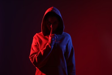 Photo of Anonymity. Woman hiding her face on dark red background