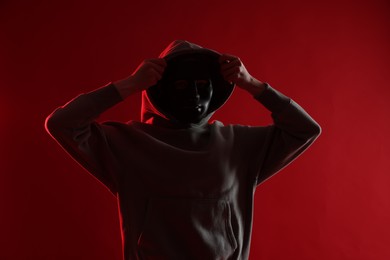 Photo of Anonymity. Woman wearing mask on red background