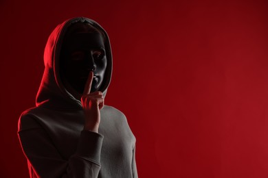 Photo of Anonymity. Woman wearing mask on red background, space for text