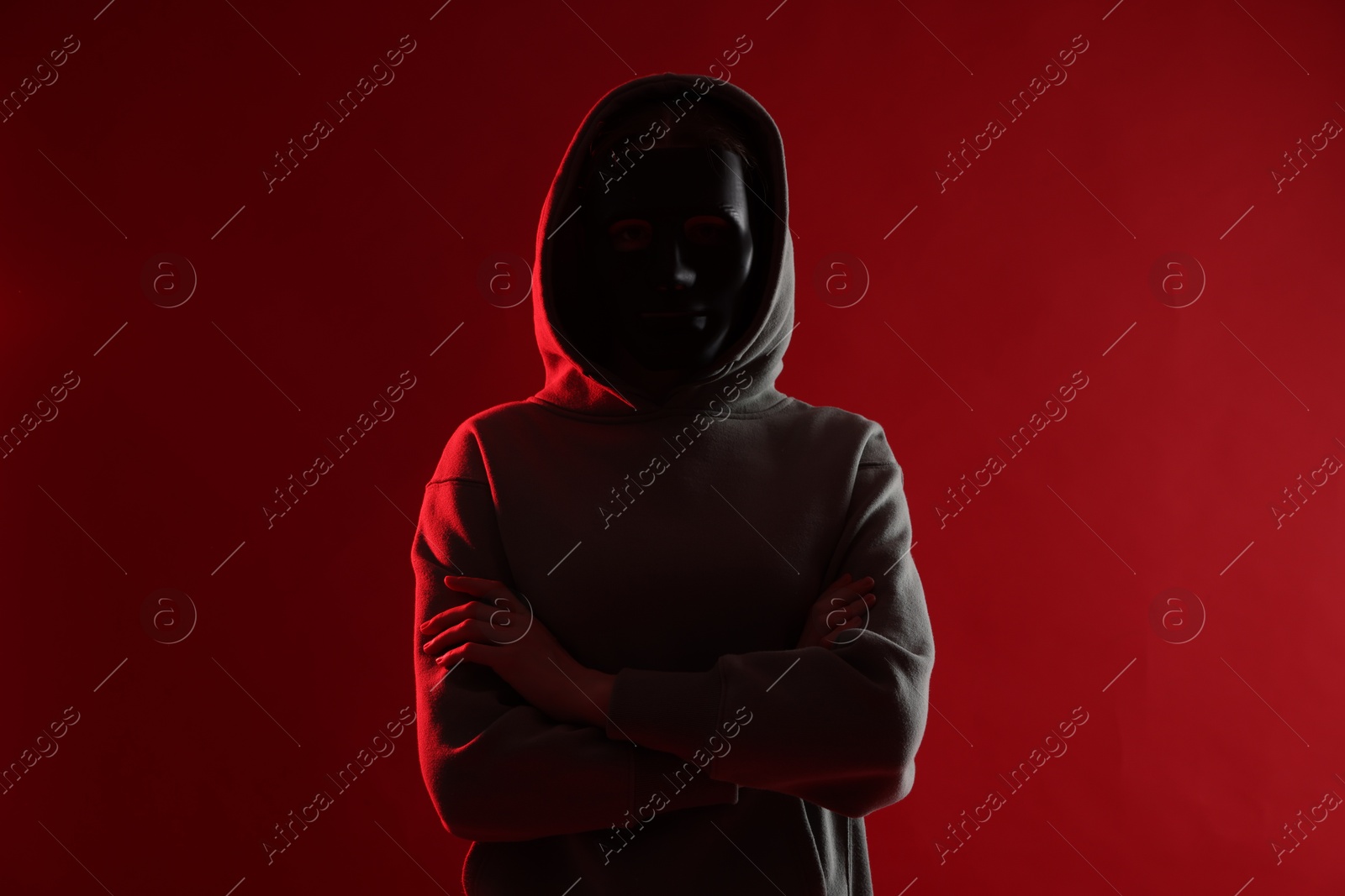 Photo of Anonymity. Woman wearing mask on red background