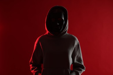 Photo of Anonymity. Woman wearing mask on red background