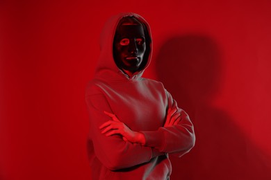 Photo of Anonymity. Woman wearing mask on red background