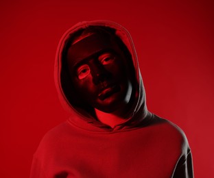 Photo of Anonymity. Woman wearing mask on red background