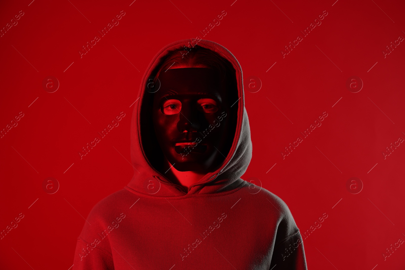 Photo of Anonymity. Woman wearing mask on red background