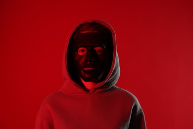 Photo of Anonymity. Woman wearing mask on red background