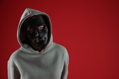 Photo of Anonymity. Woman wearing mask on red background, space for text