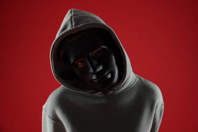 Photo of Anonymity. Woman wearing mask on red background