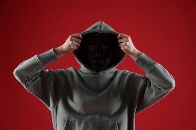 Photo of Anonymity. Woman wearing mask on red background