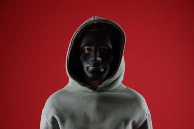 Photo of Anonymity. Woman wearing mask on red background