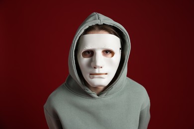 Photo of Anonymity. Woman wearing mask on dark red background