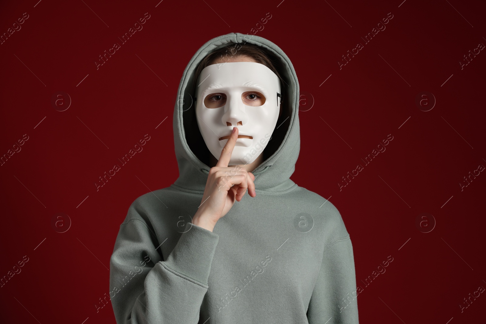 Anonymity. Woman wearing mask and showing hush gesture on dark red background Photo of Anonymity. Woman wearing mask and showing hush gesture on dark red background