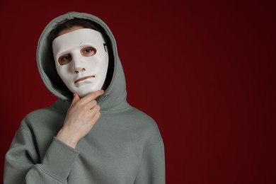 Photo of Anonymity. Woman wearing mask on dark red background, space for text