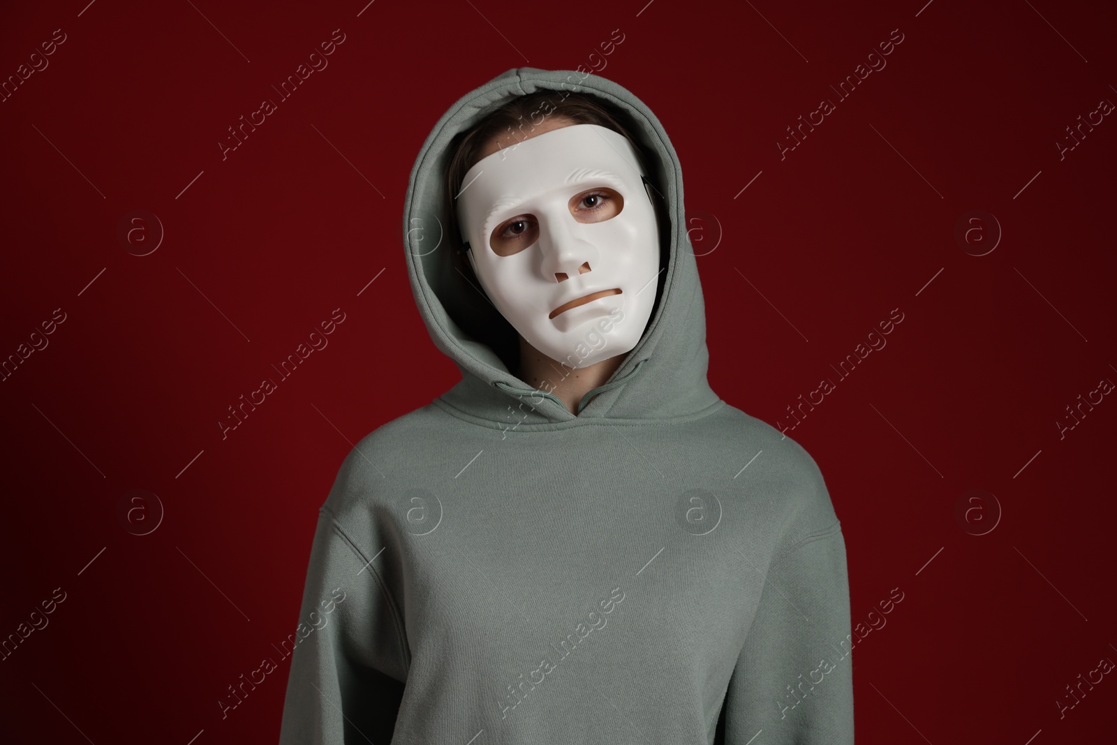Anonymity. Woman wearing mask on dark red background Photo of Anonymity. Woman wearing mask on dark red background