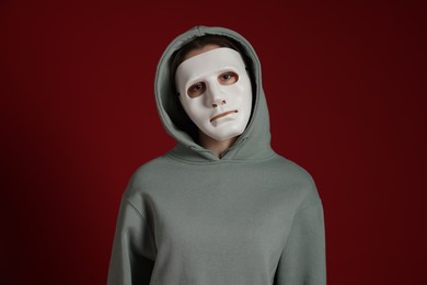 Photo of Anonymity. Woman wearing mask on dark red background