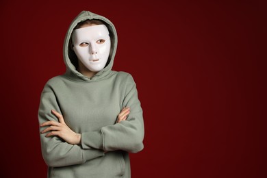 Photo of Anonymity. Woman wearing mask on dark red background, space for text