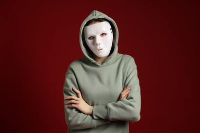 Photo of Anonymity. Woman wearing mask on dark red background