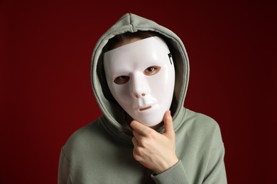 Photo of Anonymity. Woman wearing mask on dark red background