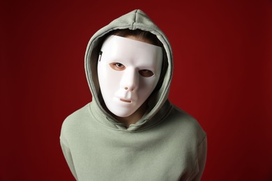 Photo of Anonymity. Woman wearing mask on dark red background