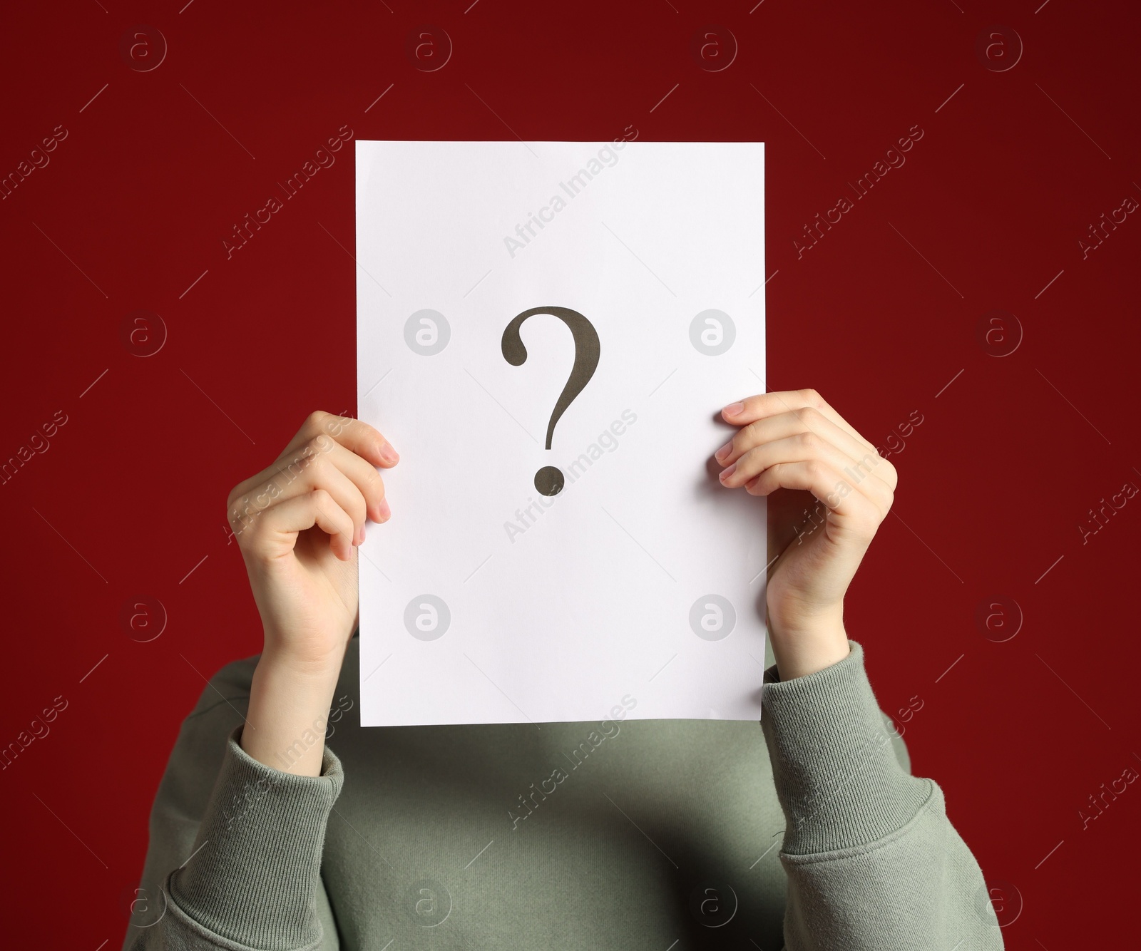 Anonymity. Woman hiding behind paper sheet with question mark on dark red background Photo of Anonymity. Woman hiding behind paper sheet with question mark on dark red background