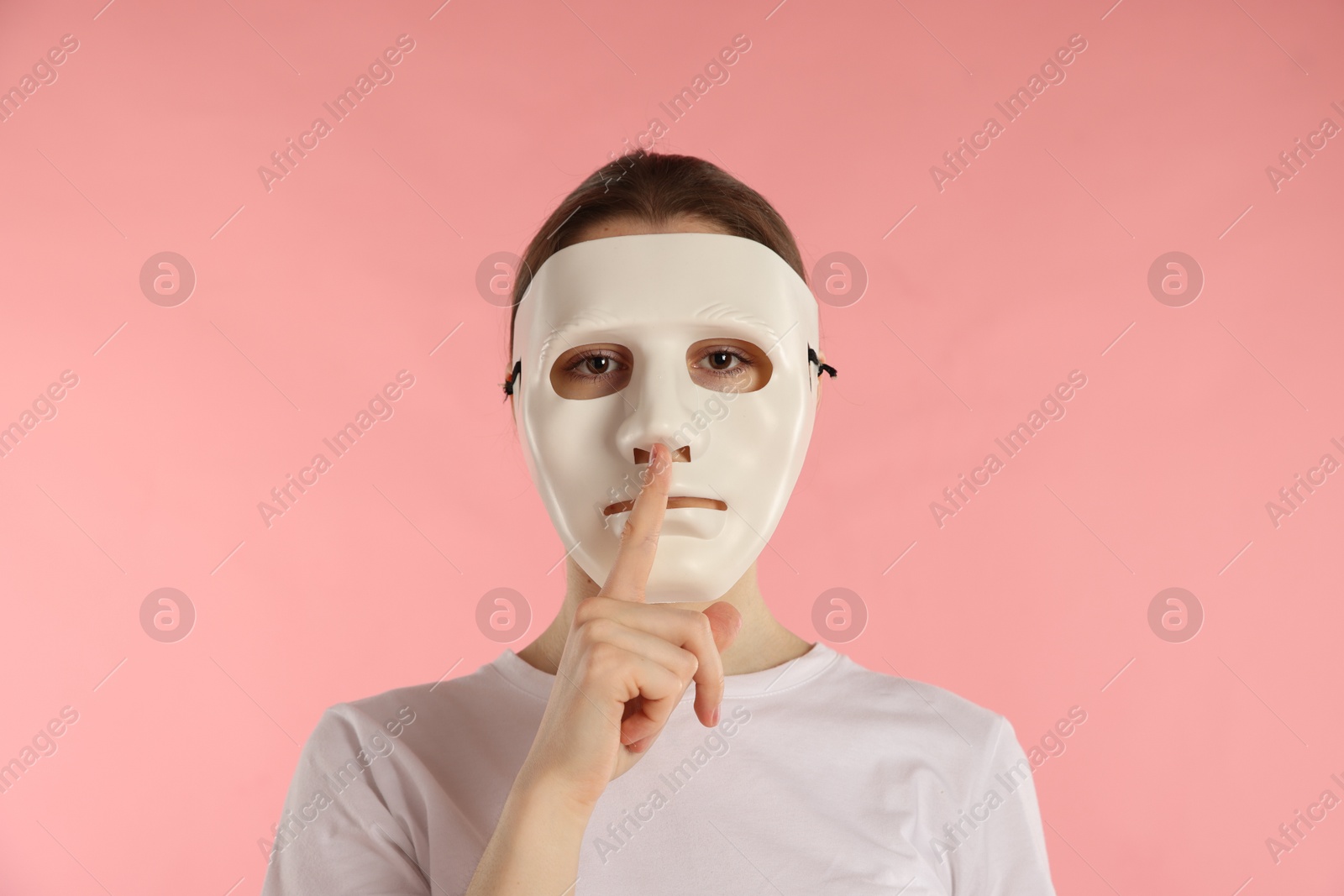 Anonymity. Woman wearing mask and showing hush gesture on pink background Photo of Anonymity. Woman wearing mask and showing hush gesture on pink background