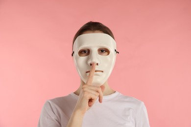 Photo of Anonymity. Woman wearing mask and showing hush gesture on pink background