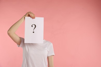 Photo of Anonymity. Woman hiding behind paper sheet with question mark on pink background, space for text