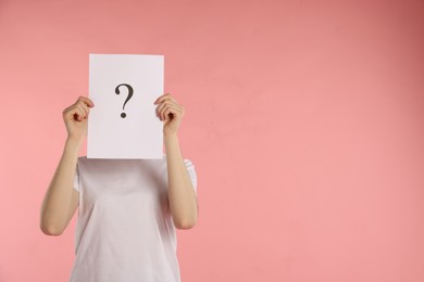 Photo of Anonymity. Woman hiding behind paper sheet with question mark on pink background, space for text