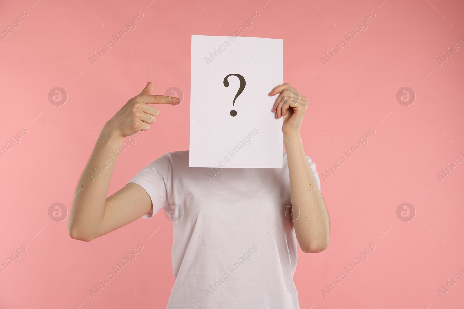 Anonymity. Woman hiding behind paper sheet with question mark on pink background Photo of Anonymity. Woman hiding behind paper sheet with question mark on pink background