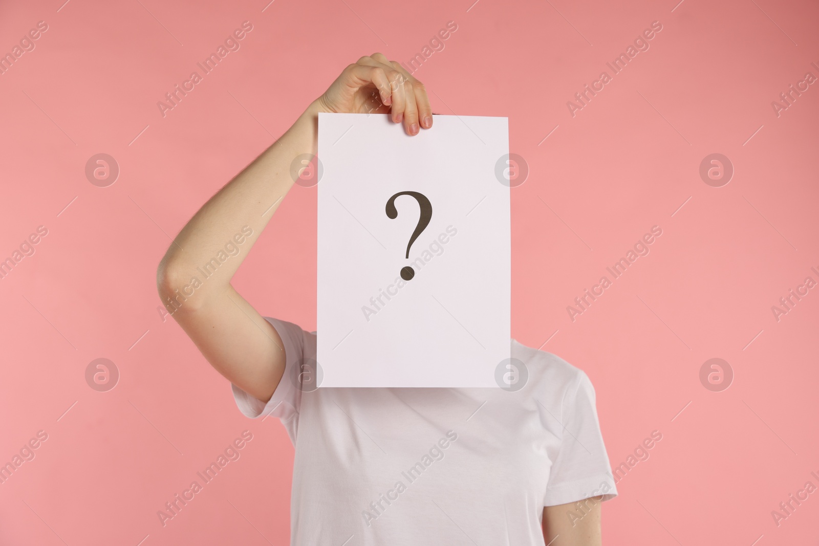 Anonymity. Woman hiding behind paper sheet with question mark on pink background Photo of Anonymity. Woman hiding behind paper sheet with question mark on pink background